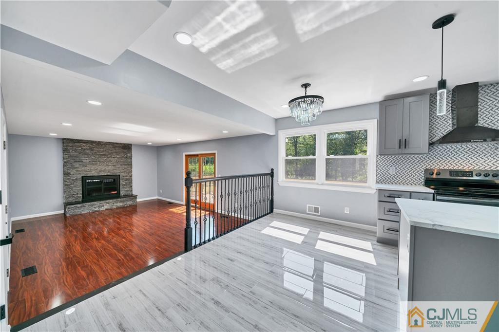 Open kitchen and living area with a marble-look island, stone fireplace, and contrasting wood floors.