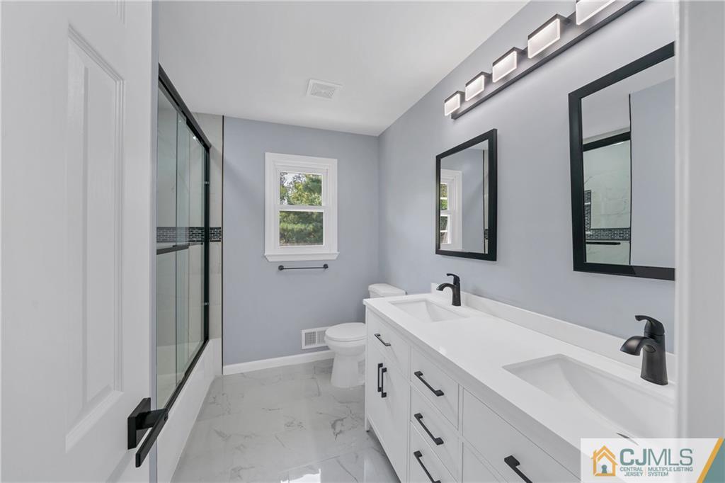 Bathroom with a long double-sink vanity, black fixtures, and a glass-enclosed shower.