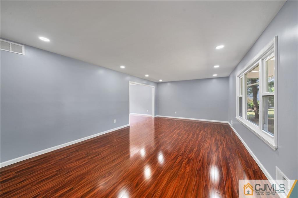 Empty living room with glossy reddish-brown hardwood floors, gray walls, and large windows.