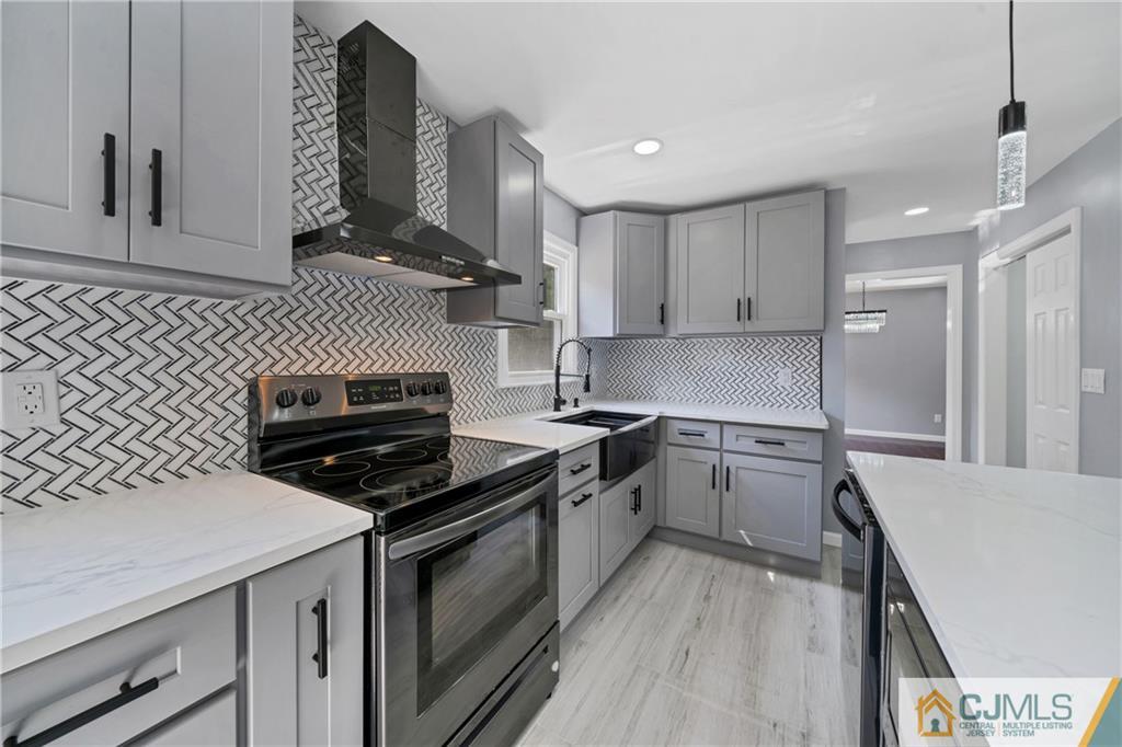 Kitchen with gray cabinets, a herringbone tile backsplash, white counters, and a black range.