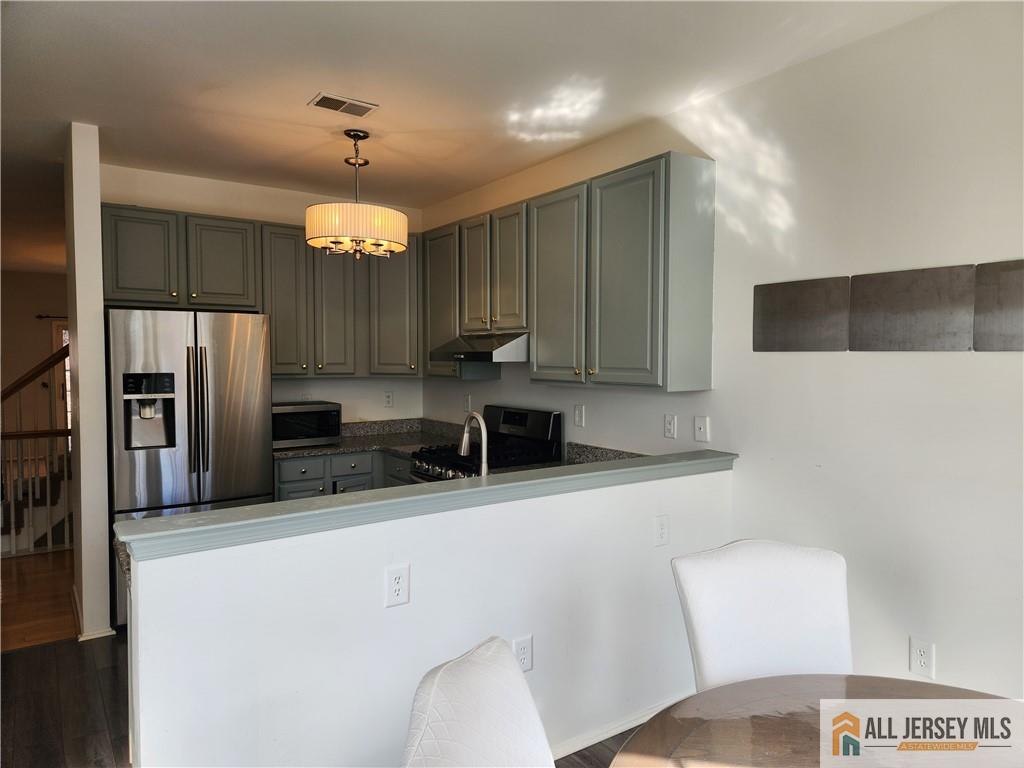 Kitchen with gray-green cabinets, stainless-steel appliances, and a white breakfast bar.