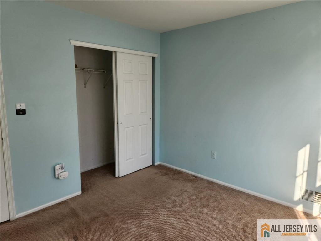 Empty bedroom with light blue walls, beige carpet, and a partially open closet.