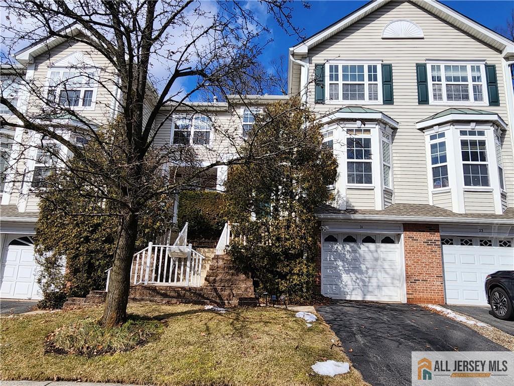 Beige townhouse with green shutters, brick accents, and an attached garage behind a leafless tree.