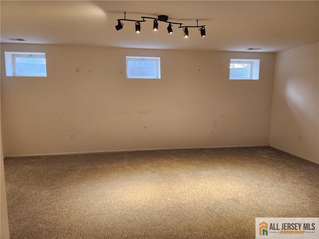 Vacant carpeted room with three high-set windows and black track lighting.