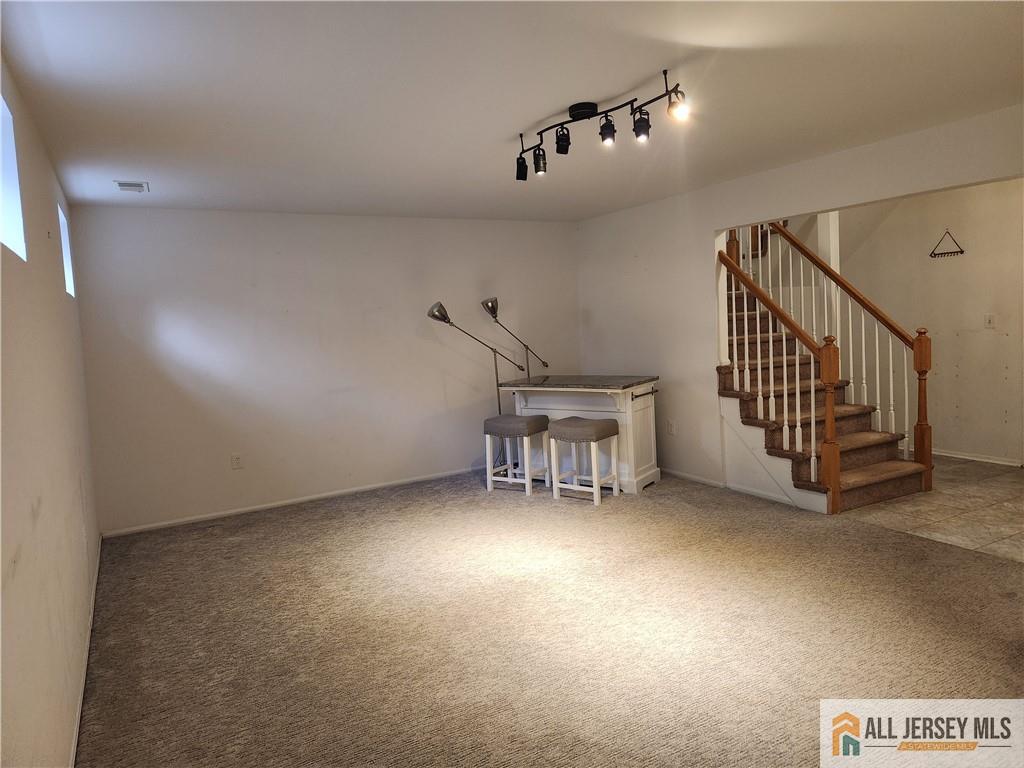 Open carpeted living area with a small counter and two stools beside a carpeted staircase.