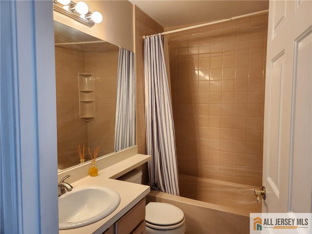 Bathroom with tan tiled tub and striped shower curtain beside a vanity and sink.
