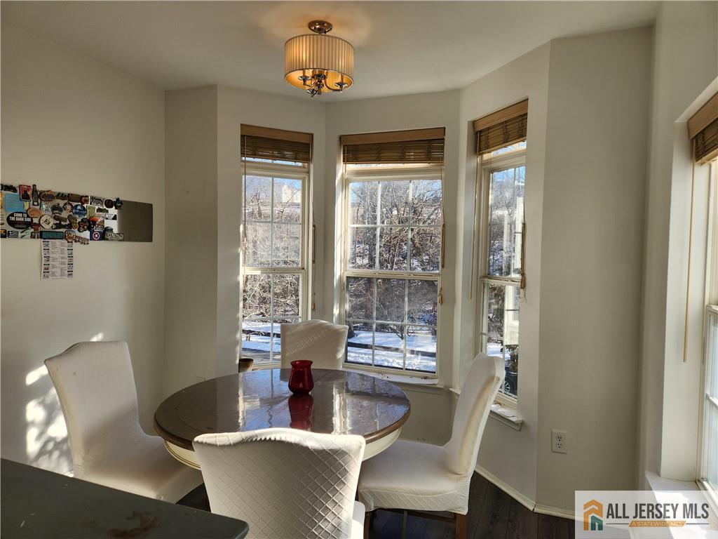 Dining area with a round table, white chairs, and bay windows overlooking a snowy, wooded view.