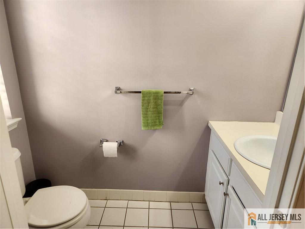 Bathroom with a white toilet and vanity, gray walls, tiled floor, and a green towel.
