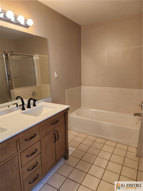 Bathroom with a wood vanity and black faucet beside a bathtub with tiled surround.