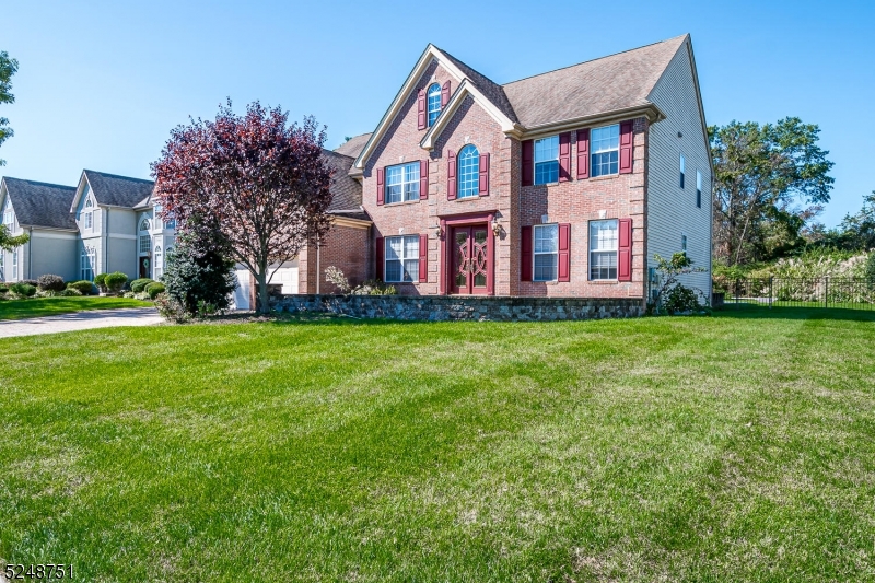 Two-story brick home with red shutters, a steep gabled roof, and a broad front lawn.