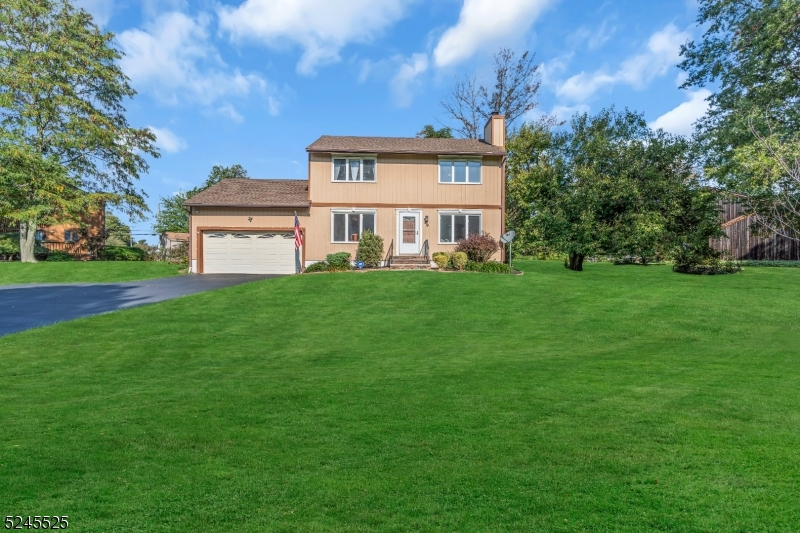 Two-story tan home with an attached garage, driveway, and expansive front lawn.
