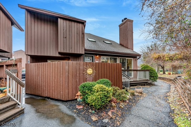 Brown-sided home with a fenced patio, small deck, and curved paved walkway.