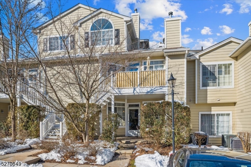 Beige multi-story home with a second-floor balcony, exterior stairs, and snow patches in the yard.