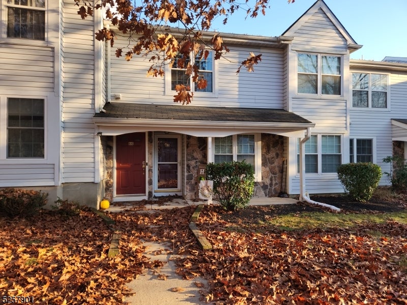 Two-story white-sided home with stone entry, red door, and a leaf-covered front yard.