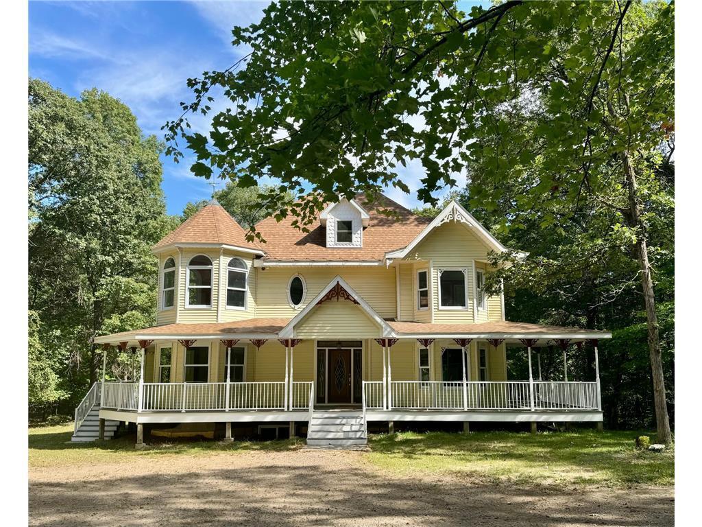 Pale yellow Victorian house with a broad white porch and mature trees.