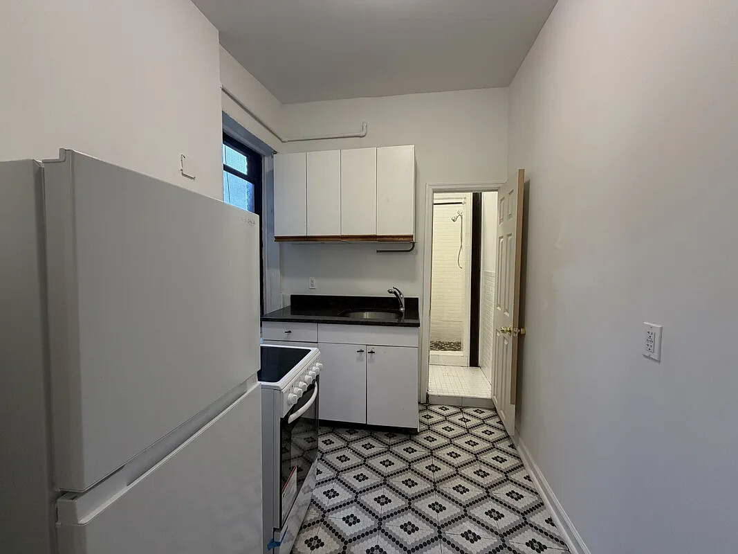 Narrow kitchen with white cabinets, black countertop, and geometric black-and-white floor tiles.