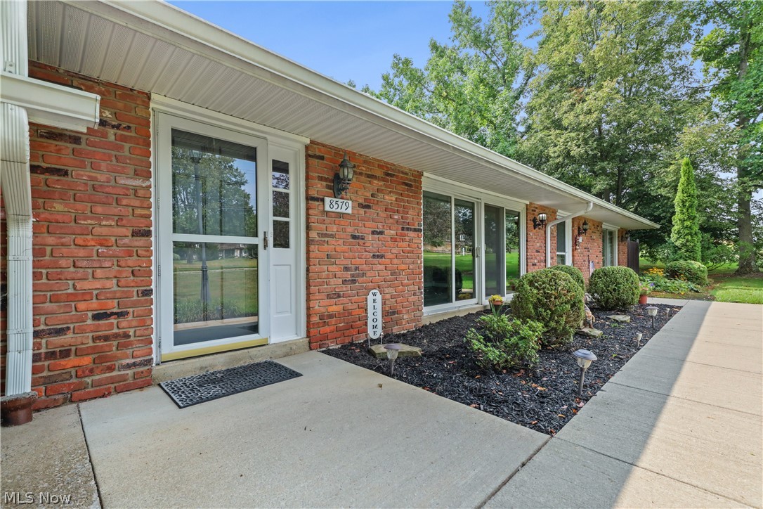 Red brick home entrance with white trim, landscaped shrubs, and house number 8579.