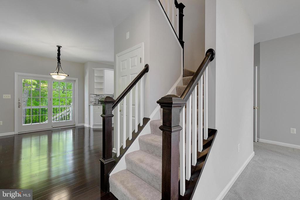 Carpeted staircase with dark wood railings beside a bright, open entry with hardwood floors.