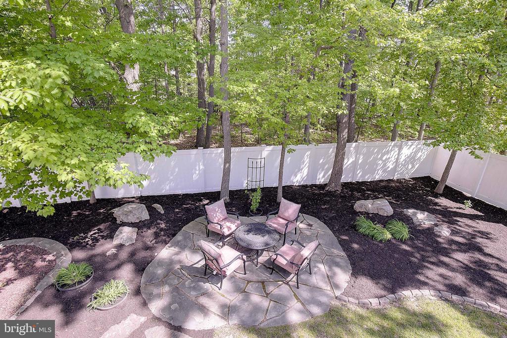 Stone backyard patio with a round table and pink chairs beneath mature trees.