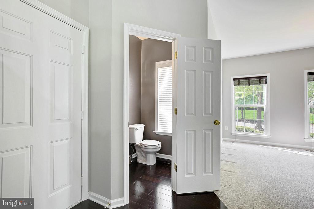 Half bathroom with dark tile flooring opens onto a bright carpeted room with large windows.