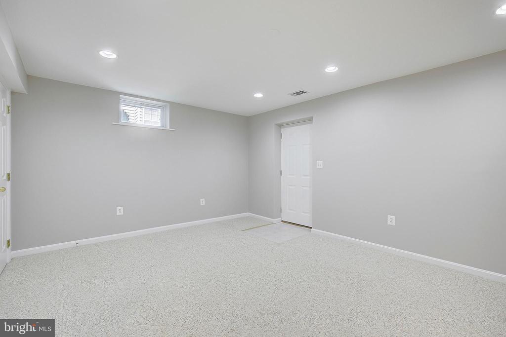Empty carpeted room with gray walls, recessed lights, a small high window, and a white door.