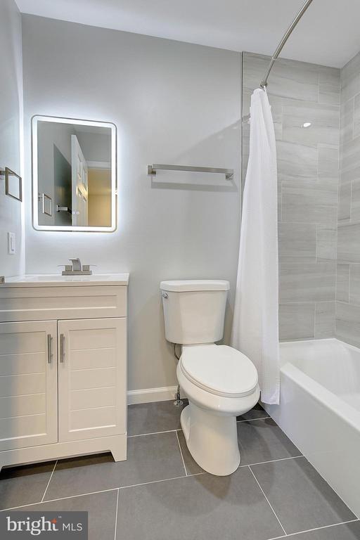 Bathroom with a white vanity and toilet beside a bathtub with gray tile surround.