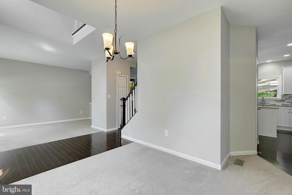 Open living and dining area with light carpet, dark wood flooring, a staircase, and kitchen beyond.