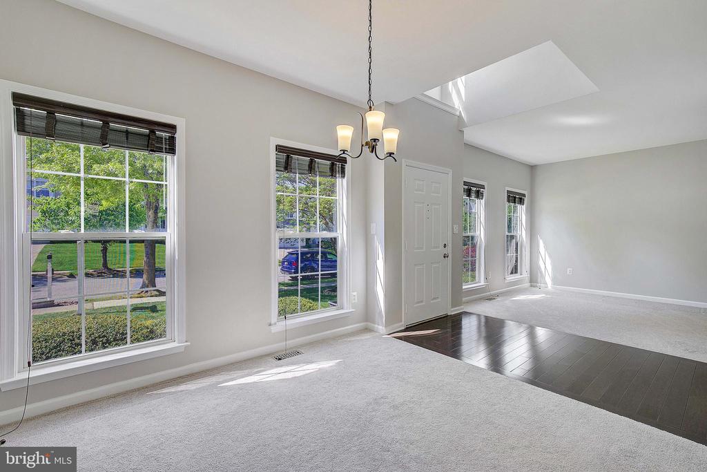 Bright vacant living room with a chandelier, skylight, and windows overlooking the front yard.
