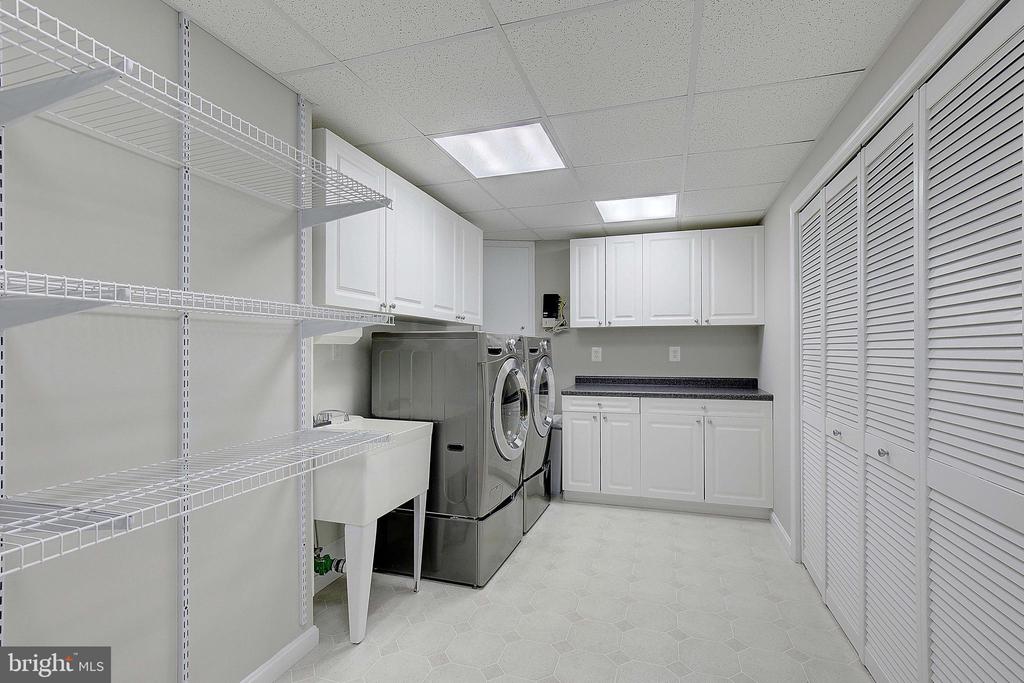 Laundry room with front-loading washer and dryer, utility sink, white cabinets, and wire shelving.