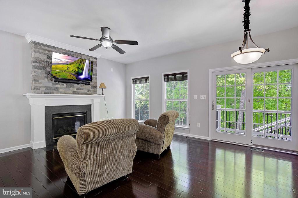Living room with stone-surround fireplace, two upholstered chairs, and glass doors to a leafy deck.