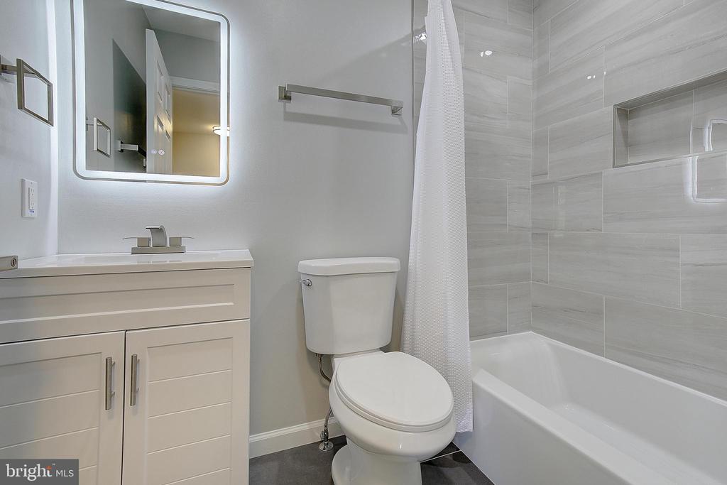 Bathroom with a white vanity, toilet, and bathtub surrounded by large gray tiles.
