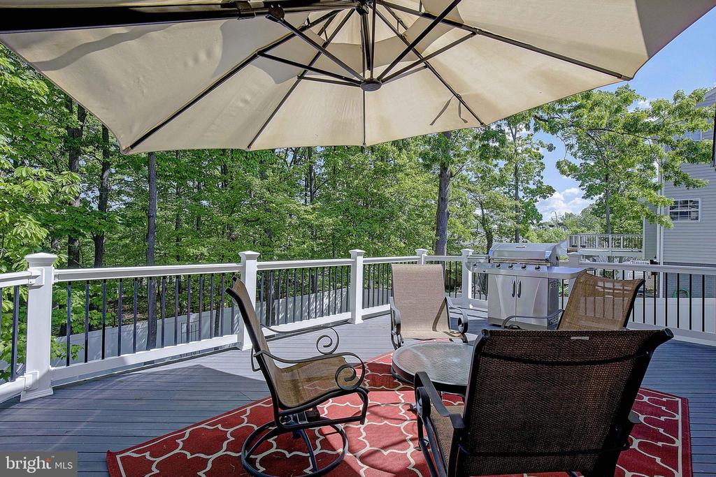 Furnished deck with patio seating, a large umbrella, and grill overlooking leafy trees.