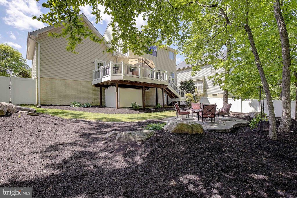Home’s rear deck and stone patio with outdoor seating beneath mature trees.