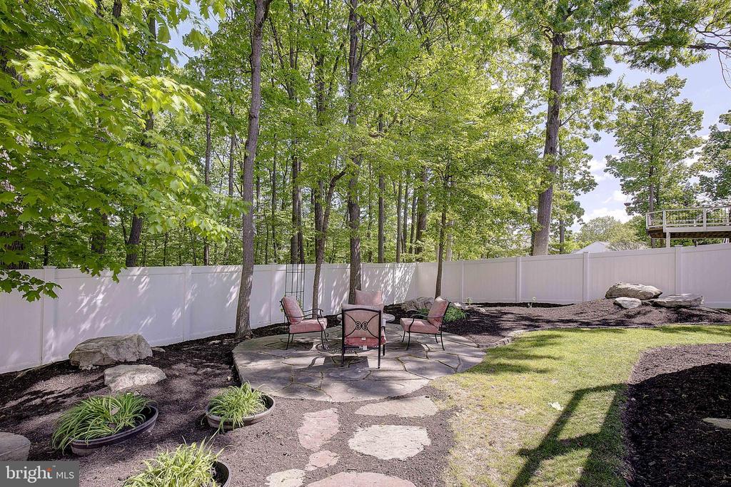 Backyard patio with seating, stone stepping path, white privacy fence, and mature trees.