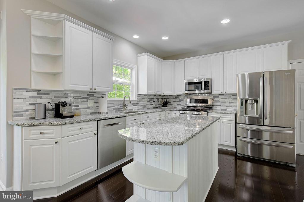 Kitchen with white cabinetry, granite counters, a large peninsula, and stainless steel appliances.