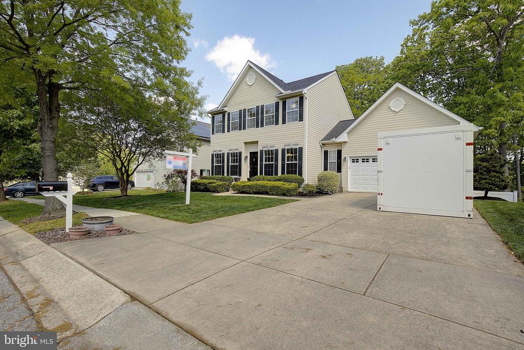 Two-story beige house with black shutters, attached garage, and a large white trailer in the driveway.