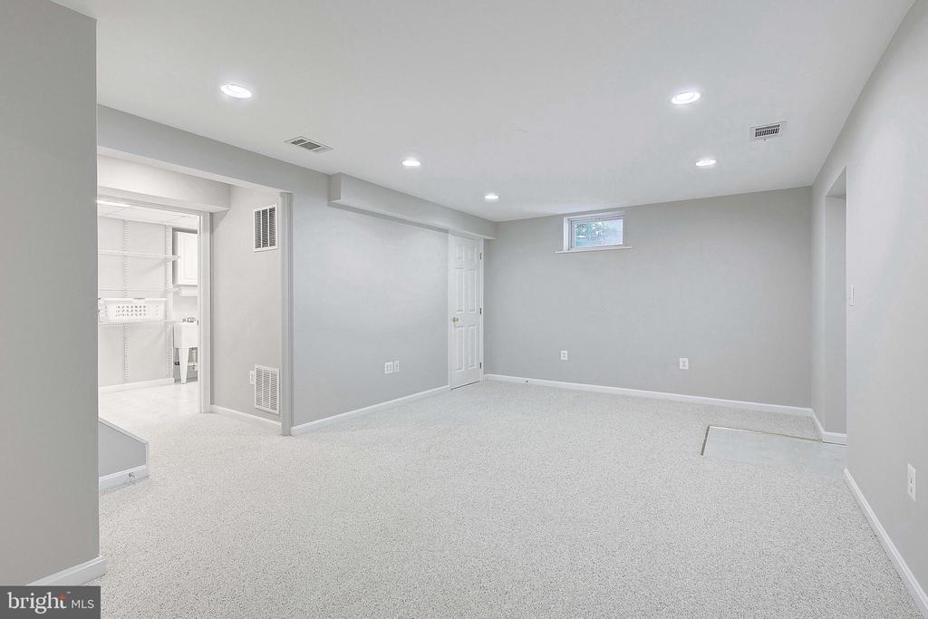 Empty carpeted basement room with recessed lights and an adjoining laundry area.