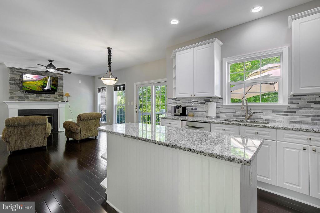 Open kitchen with a large granite island and white cabinetry beside a living area with a fireplace.