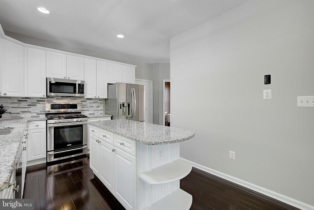 Kitchen with white cabinets, stainless appliances, and a granite island with curved seating.