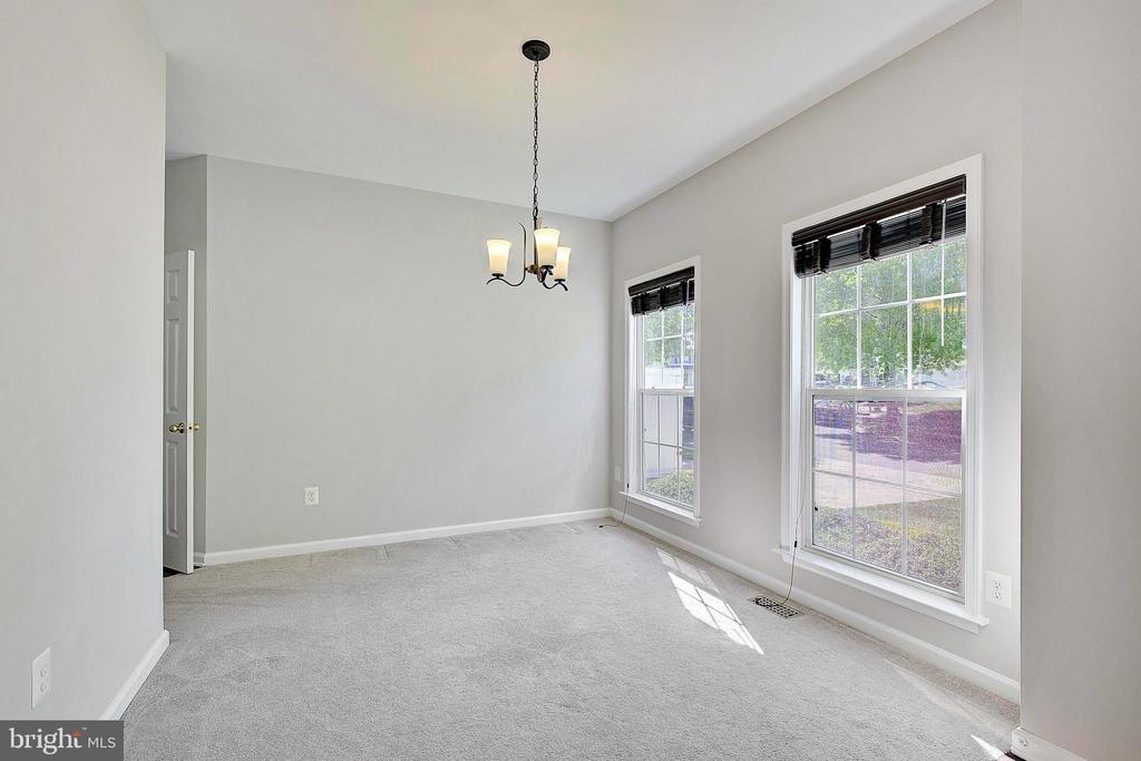 Empty dining room with gray carpet, a chandelier, and two large windows.