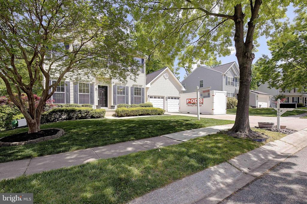Two-story house with an attached garage, shaded front lawn, and PODS container in the driveway.