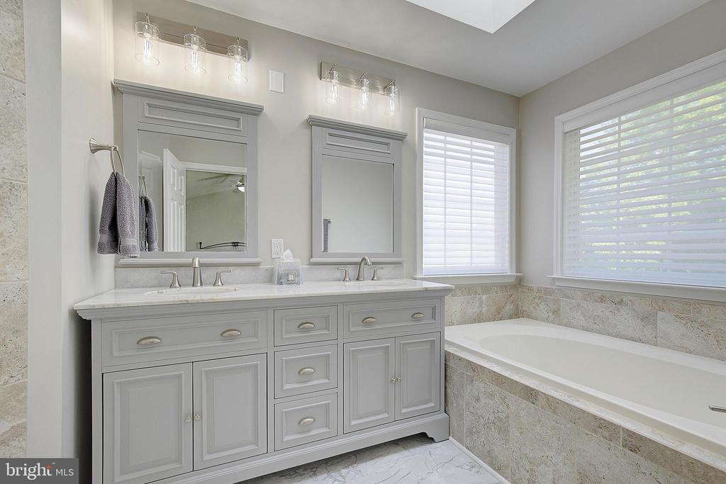 Bathroom with a gray double vanity and a tiled soaking tub beneath shuttered windows.