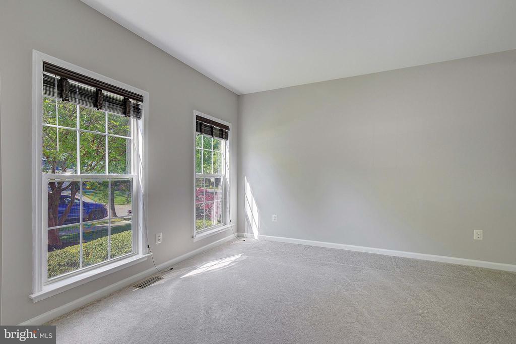 Empty carpeted bedroom with gray walls, two windows, and sunlight across the floor.