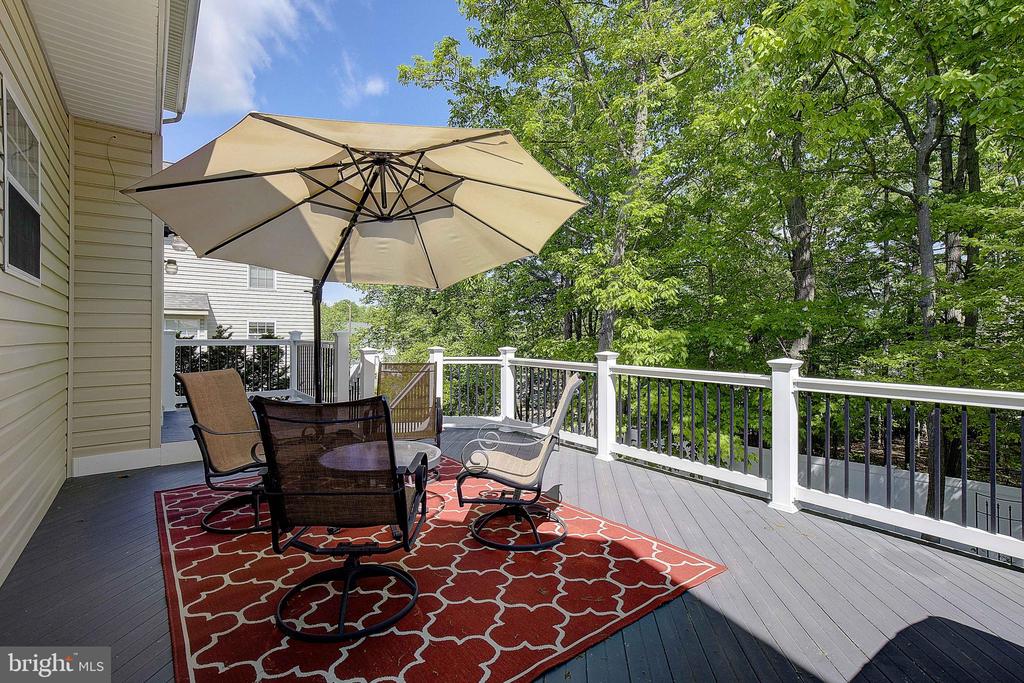 Furnished deck with umbrella and red rug overlooking leafy trees.