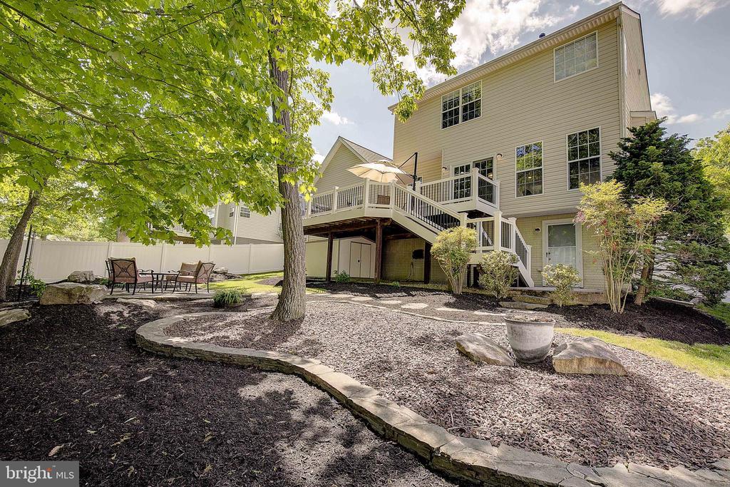 Home’s rear exterior with a raised deck and landscaped garden beneath mature trees.
