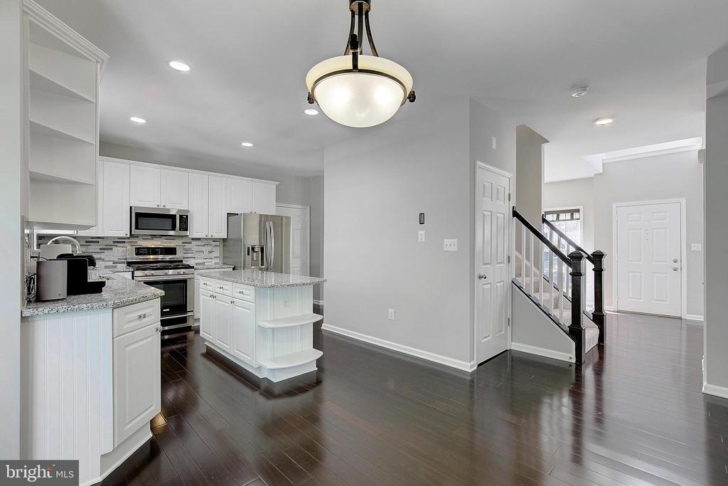 White kitchen with stainless steel appliances and granite counters, opening to a foyer with a staircase.
