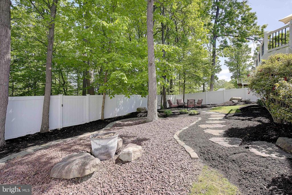 Backyard with mature trees, white privacy fence, curved stepping-stone path, and patio seating.