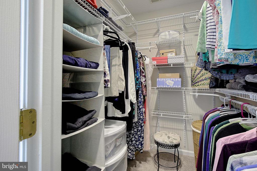 Walk-in closet with wire shelving, hanging clothes, and a small stool.