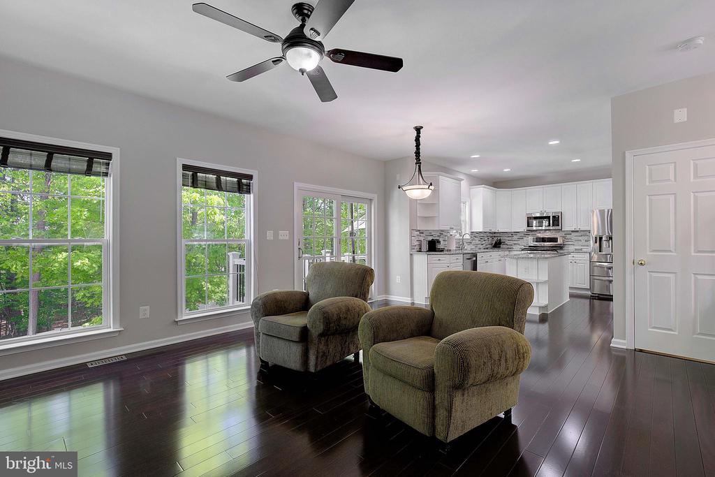 Living room with two armchairs and dark hardwood floors, opening to a white kitchen.