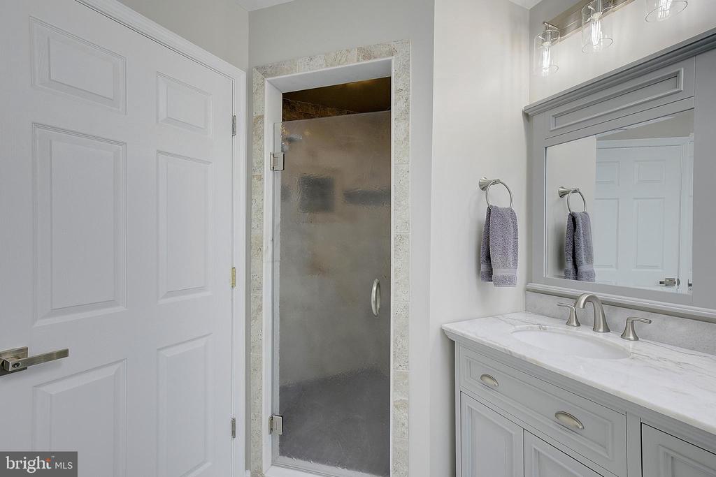 Bathroom with a frosted-glass shower and white vanity with marble-look countertop.